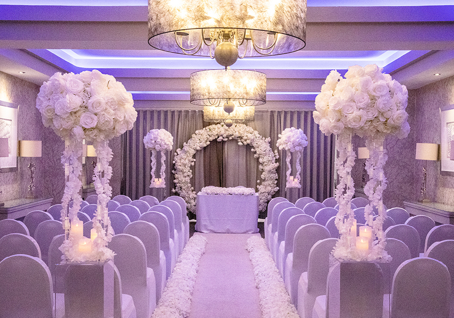 White ceremony room with purple-hued lighting and white rose arch and bouquets